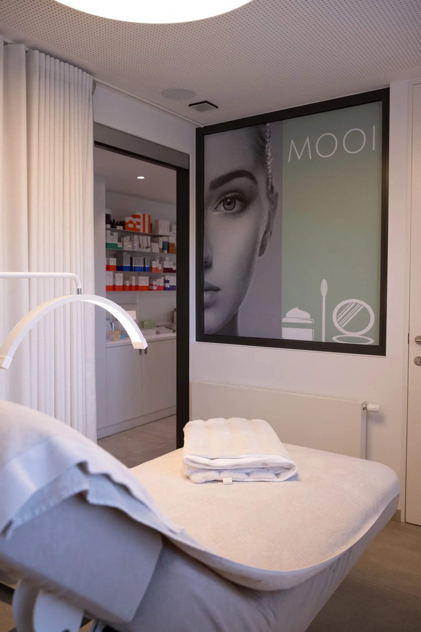 Behandelcabine van Mooi met behandeltafel, handdoeken en de MOOI-poster aan de muur